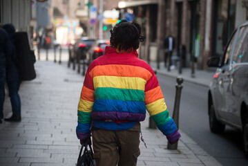 Strasbourg - France - 4 March 2023 - portrait on back view of young woman wearing a rainbow coat walking in the street