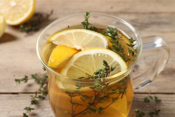Glass cup of aromatic herbal tea with thyme and lemon on wooden table, closeup
