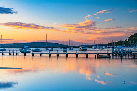 Sunrise waterscape with boats, wharf, clouds and reflections