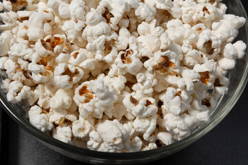 Glass and transparent bowl of fried popcorn on black background.