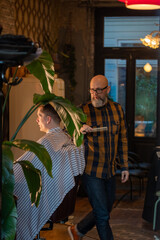 Bearded male barber cutting hair of a client in a barbershop. High quality photo