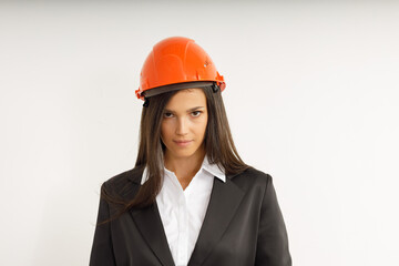Beautiful model in orange construction helmet. Portrait of happy smiling brunette girl with long hair, dressed in strict suit. Studio shot of young business woman on isolated white background.