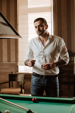Handsome man is posing with billiard stick on the billiard table in the bar or salloon