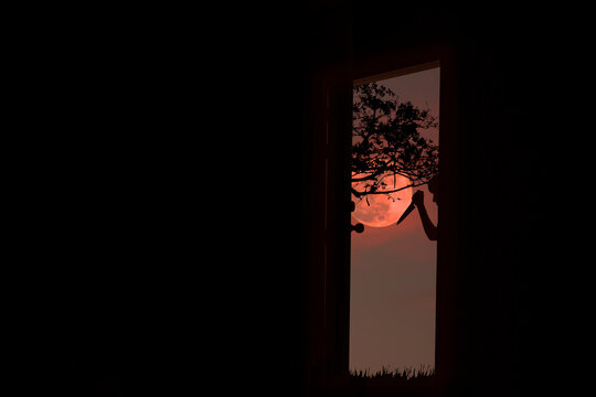 Silhouette of scary man holding knife at door in red moon night