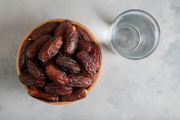 Glass of water with a bowl of date fruit on bright background