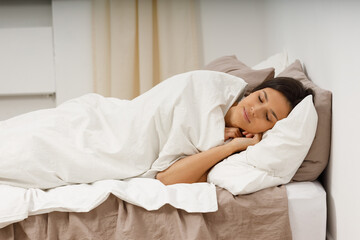 Healthy young woman covers blanket sleeping with closed eyes on bed in bedroom.