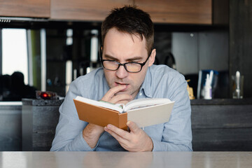 leisure, literature and people concept reading book at home. reader is reading interesting novel. student is studying textbook. guy is holding a book in his hand. guy is passionate about reading