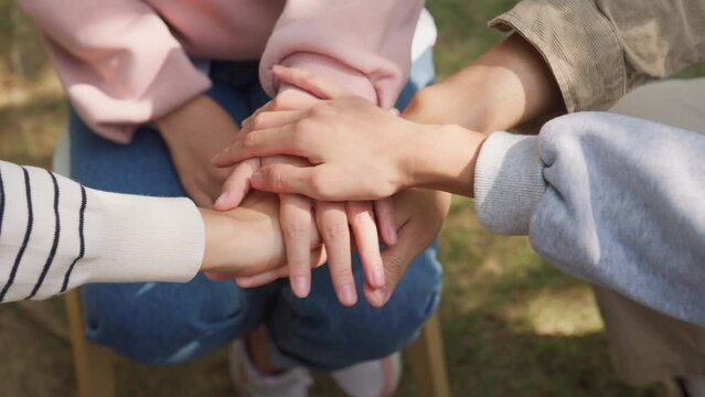 Close-up of diverse multiracial men and women group sit in circle hold hands together hope for help people in park. Support and understand at psychological therapy session, PTSD Mental health concept.