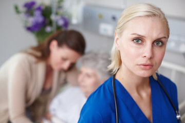 I hate this part of my job. Portrait of a serious young nurse with a senior patient and her daughter in the background.