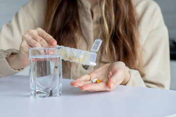 A woman pours pills into her hand from a medical organizer container. Daily intake of medicines and...