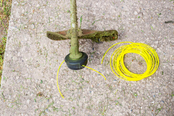 A lawn mower with fishing line after cutting the grass and a roll of new fishing line nearby. Replacement of consumables on the trimmer