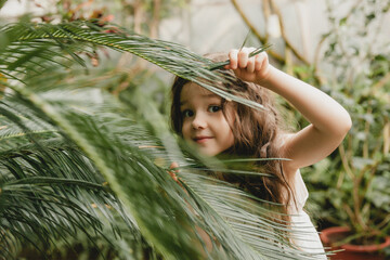 Little girl in the botanical garden. a girl in a white dress laughs near palm leaves.