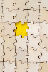 Assembled puzzle background. One missing wooden puzzle on a yellow background. The concept of completing a case. Vertical Photo.