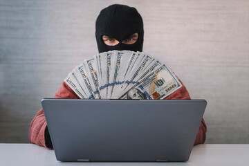 a male thief holds dollars in his hand. using laptop computer for password hacking activities....