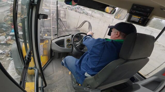 Fast motion shot of loading a truck and transporting waste materials with a front loader at a landfill site, inside driver cabin view.