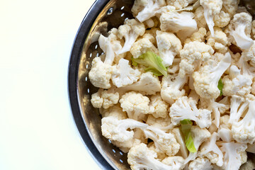 Cauliflower florets are removed and placed in a colander ready for cooking. View from above.