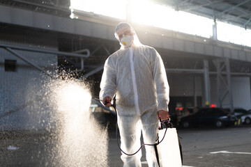 Man dressed white protective overalls spraying surface antibacterial sanitizer sprayer during...