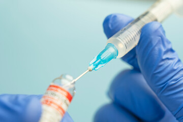 Macro of a hypodermic syringe or needle being filled with mRNA vaccine from bottle against blue...