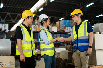Asian warehouse workers team shaking hands together in the storage warehouse, feeling happy and smiling. teamwork at warehouse storage department.