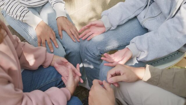 Close-up hands of diverse multiracial male and female group sit circle explain tell story sharing together in park. Support and understand at psychological therapy session, PTSD Mental health concept.