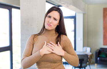 young adult pretty woman looking sad, hurt and heartbroken, holding both hands close to heart, crying and feeling depressed