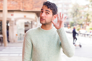 young hispanic man looking serious and curious, listening, trying to hear a secret conversation or...