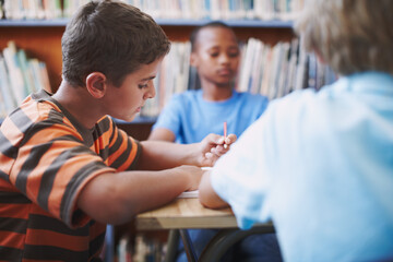 Obraz premium Enjoying his creative writing. A young boy concentrating on his work while at the library with his classmates.