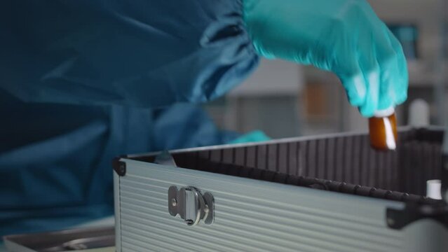Closeup of unrecognizable gloved microbiologist opening silver suitcase with radioactive test samples in glass bottles, conducting experiment in chemical laboratory