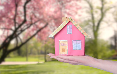 Cute model home on a female hand on blurred beautiful nature and springtime background. Real estate,house purchase, business conccept.
