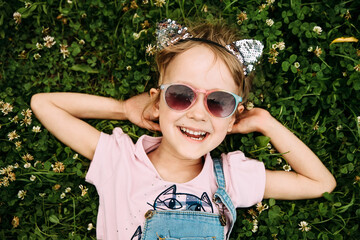 Portrait of a little girl wearing a cat ear headband lies on the grass