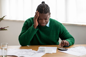 Unhappy African American Man Calculating Expenses And Bills In Office