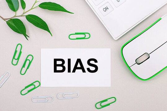 On A Light Background, A White Calculator, A Computer Mouse, Green Paper Clips, A Green Plant And A White Blank Sheet With The Text BIAS. Flat Lay.