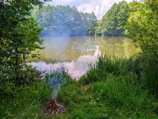 A fire burns on the shore of the pond in summer