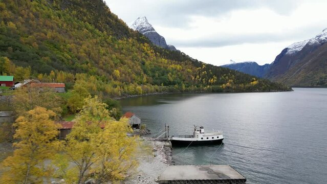 The farm Vike in Eikesdal is beautifully situated between steep mountains. An old ferry is moored at the dock. The snow has arrived on the mountain tops and the forest has its  its autumn colours