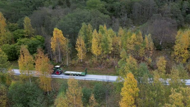 A tractor drives along a narrow Norwegian road in Western Norway. Passing Vike farm on the way to Eresfjord. Beautiful autumn colors cover the trees