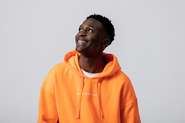 Happy delighted african american man in casual hoodie sweater pullover looking up standing over grey background in studio isolated having fun posing while shooting process.