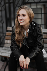 Fototapeta na wymiar Close up portrait of a beautiful smiling young blonde woman in a black leather jacket on the a city street background