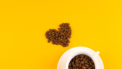 White coffee cup with beans in shape of heart. Yellow background. Copy space