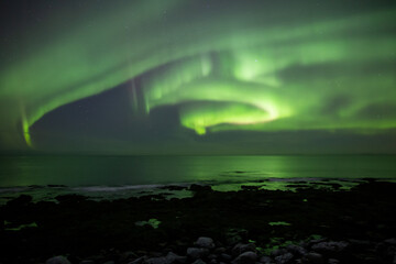 Bright winding aurora borealis over rocky beach waves Iceland