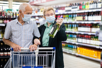 mature european spouses chooses bottle of wine in alcohol section of supermarket