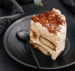 Traditional italian tiramisu cake on black plate