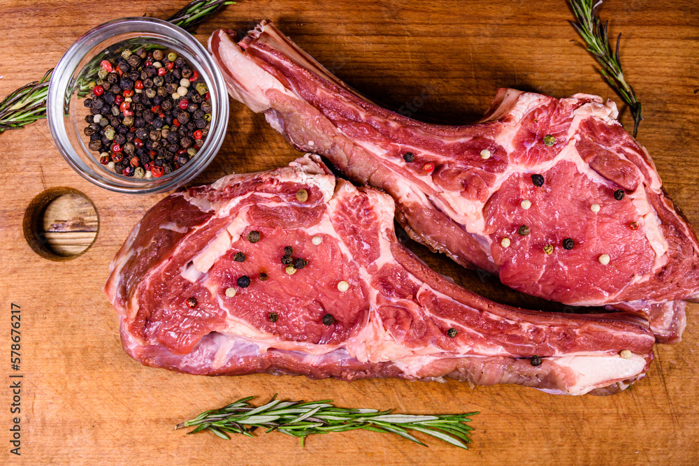 Wall mural raw ribeye steak, glass jar with spices and rosemary on cutting board. top view