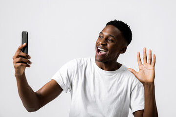 Photo of happy delighted african american black guy holding new modern smartphone in hands showing at camera expressing good emotions taking selfie photo of himself posting on social media.
