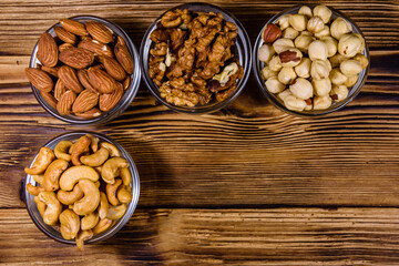 Various nuts (almond, cashew, hazelnut, walnut) in glass bowls on a wooden table. Vegetarian meal. Healthy eating concept. Top view