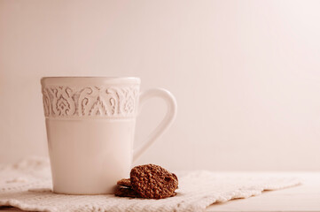 White mug and cookies on a white table dressed with a handmade crochet placemat