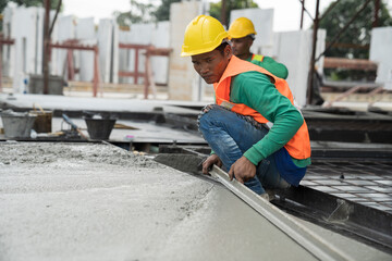 Construction technician working by leveling concrete floor to smooth. Construction worker uses long trowel spreading wet concrete pouring at construction site. Mason making smooth surface of concrete
