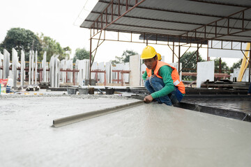 Fototapeta premium Construction technician working by leveling concrete floor to smooth. Construction worker uses long trowel spreading wet concrete pouring at construction site. Mason making smooth surface of concrete