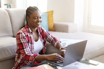 Positive black woman freelancer working from home, using pc