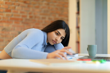 Sad teen spanish lady studying and feeling bored, sitting at table at home, free space