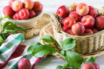 Red fresh ripe plums with water drops in wicker container on white wooden table, organic plums served for eating, healthy food and fruit  concept